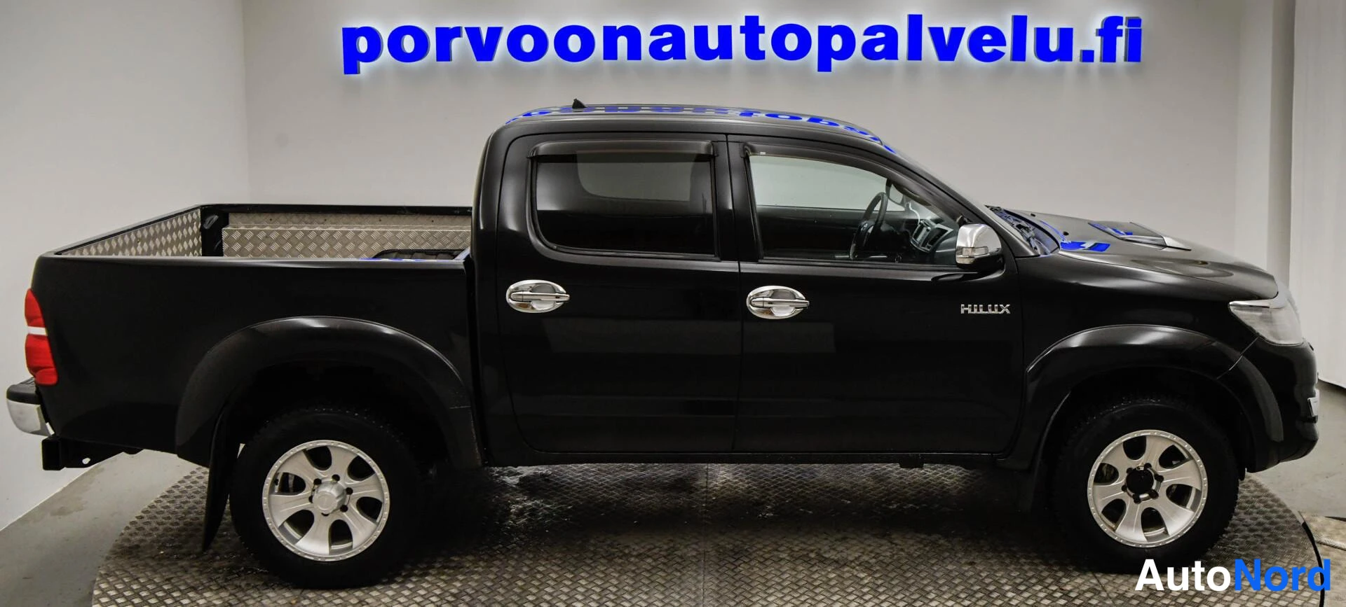 Sivulta: Mustan Toyota Hilux -avolavan sivuprofiili vasemmalta katsottuna sisätiloissa.