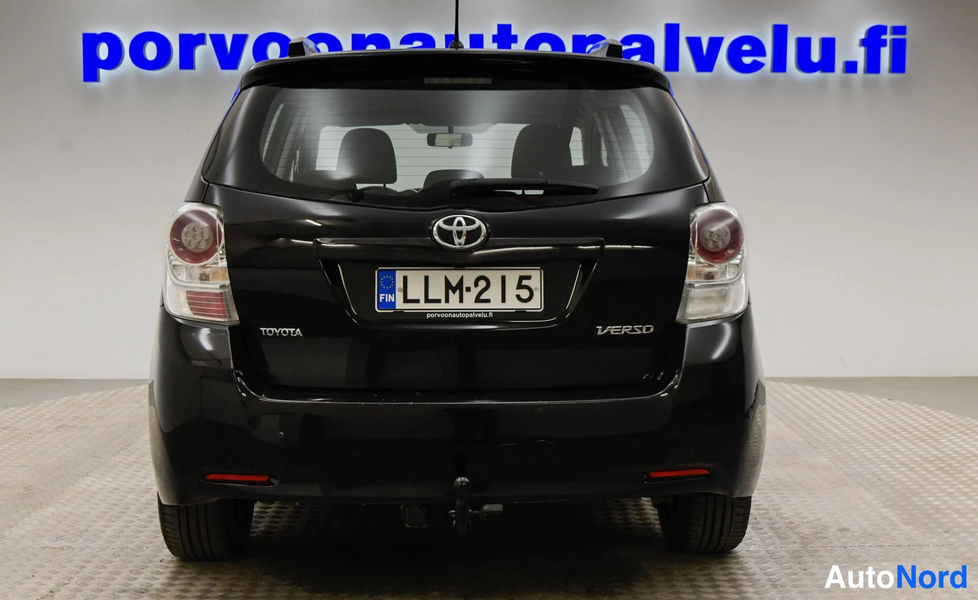Takaa: Mustan Toyota Verson suora takaosan kuva; takavalot, takaluukun kahva, Toyota- ja Verso-merkit sekä -rekisterikilpi näkyvät. Taustana mainosteksti.