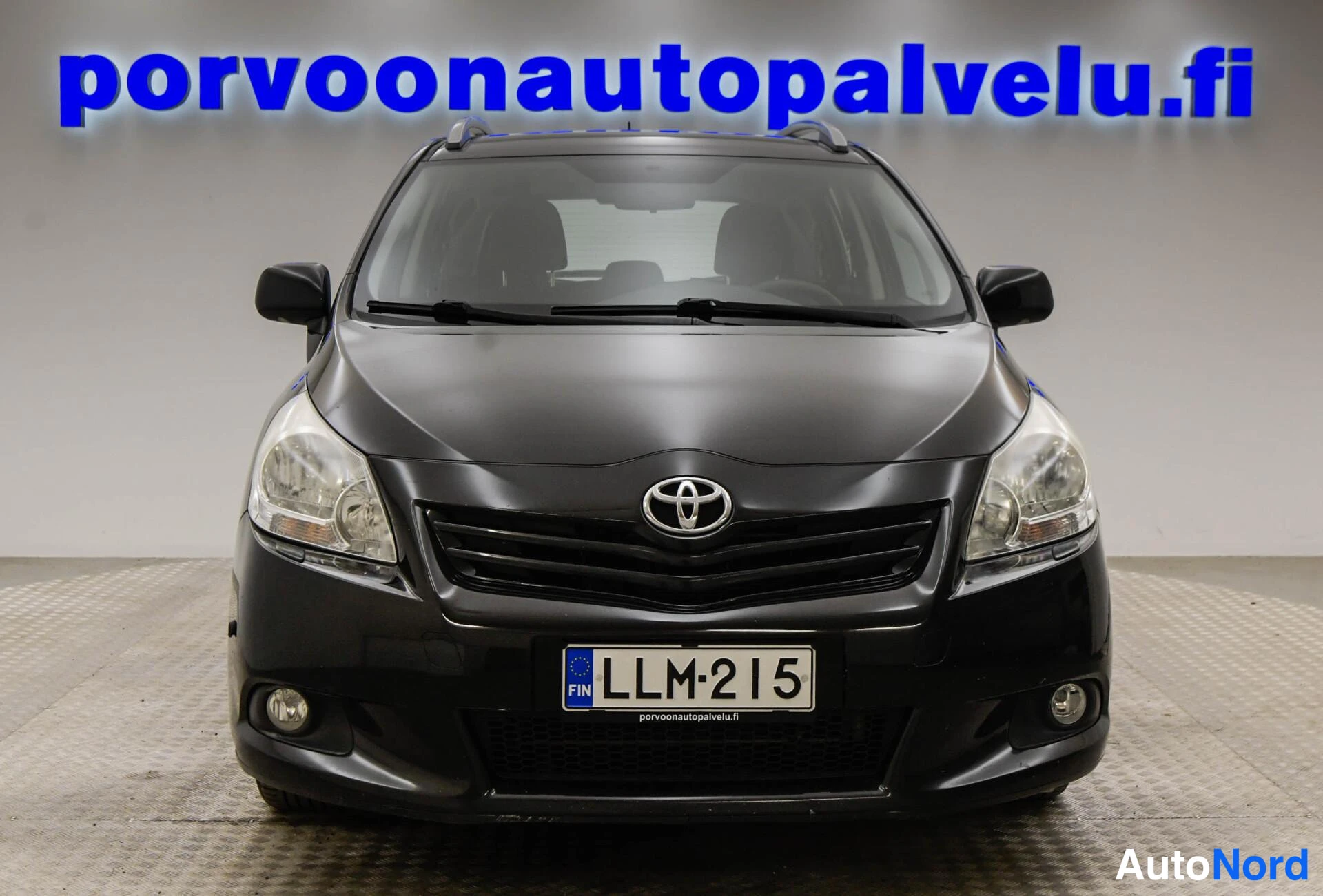 Edestä: Mustan Toyota-henkilöauton suora etunäkymä, rekisterikilpi ja sininen porvoonautopalvelu.fi-kyltti taustalla.