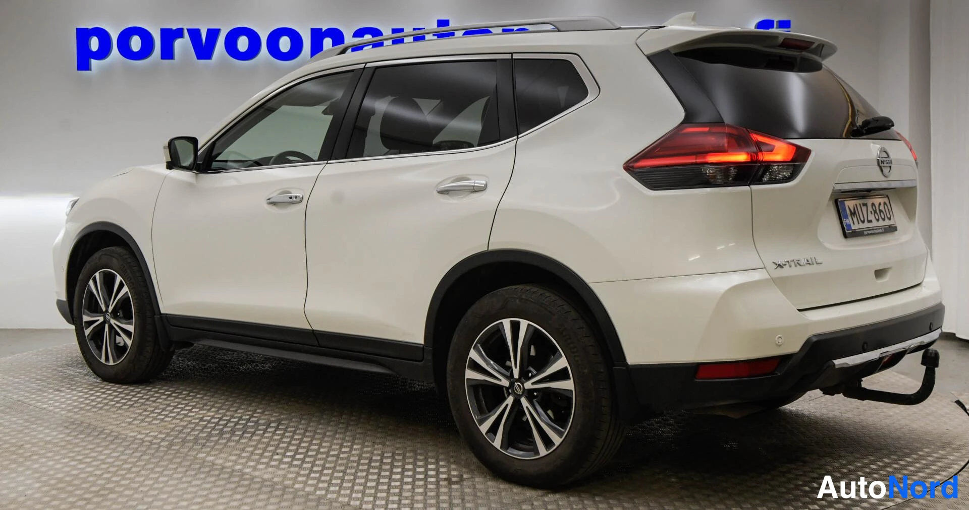 Takaviisto: Nissan X-Trail, valkoinen, takakulmanäkymä vasemmalta, rekisteritunnus, takavalojen pilkut syttyneinä, kytkimen savi/kytkysluku 'X-Trail' takaluukussa.