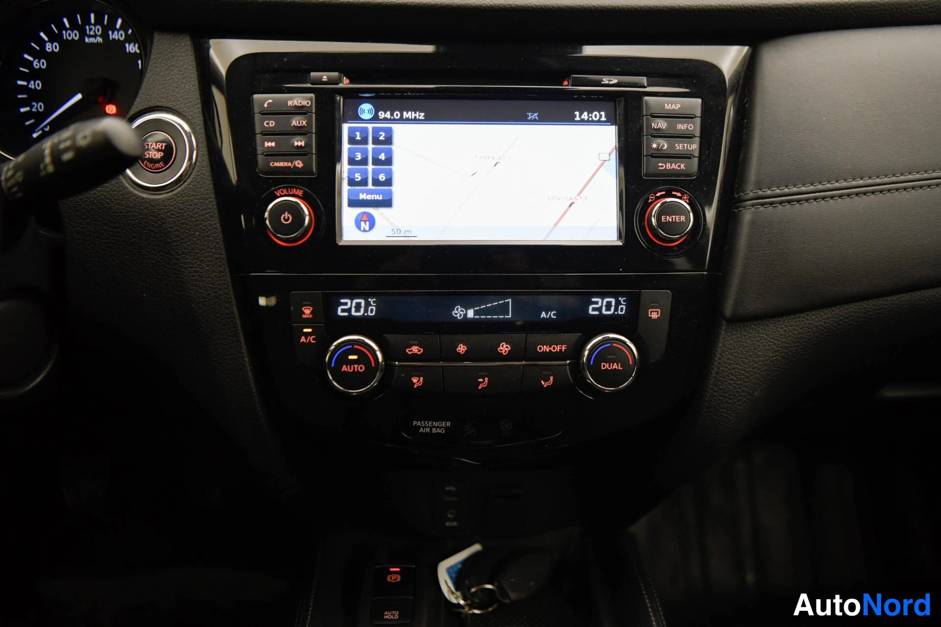 Yksityiskohta: Kojelaudan keskusta: kosketusnäyttö, jolla radio 94,0 MHz ja navigointikartta, ilmastointinapit A/C ja AUTO, DUAL-nupit sekä START STOP -käynnistyspainike.