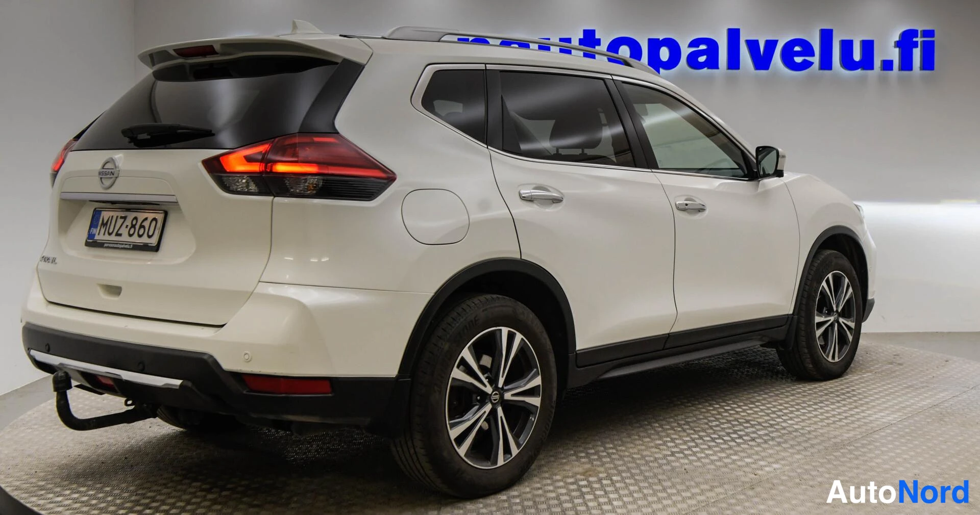 Takaviisto: Nissan X-Trail, valkoinen, takakulmanäkymä oikealta, rekisteritunnus, vetokoukku ja kattokaiteet näkyvissä.