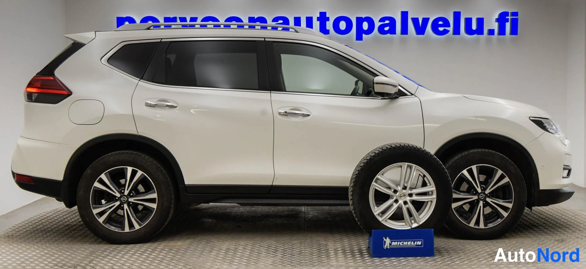 Takaviisto: Valkoinen Nissan X-Trail takakulmasta oikealta, rekalla erillinen rengas vanteella Michelin-telineessä.