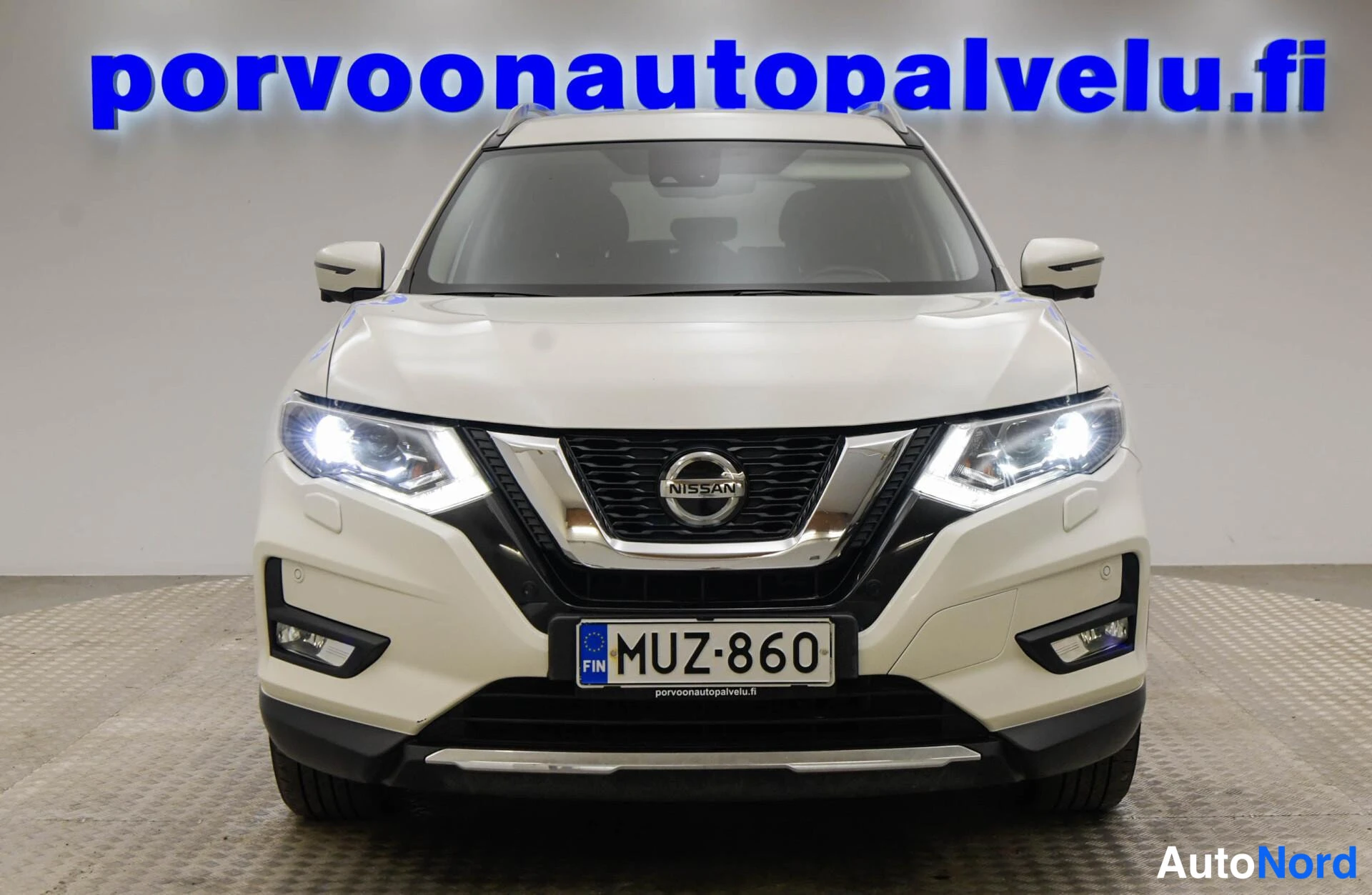 Edestä: Valkoinen Nissan X-Trail suoraan edestäpäin, Volvo-tyylinen etusäleikkö, rekisterikilpi.