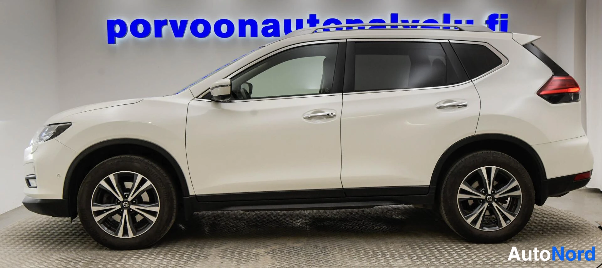 Etuviisto, nokka vasemmalle: Valkoinen Nissan X-Trail etukulmasta vasemmalta, sivuprofiili näkyvissä.