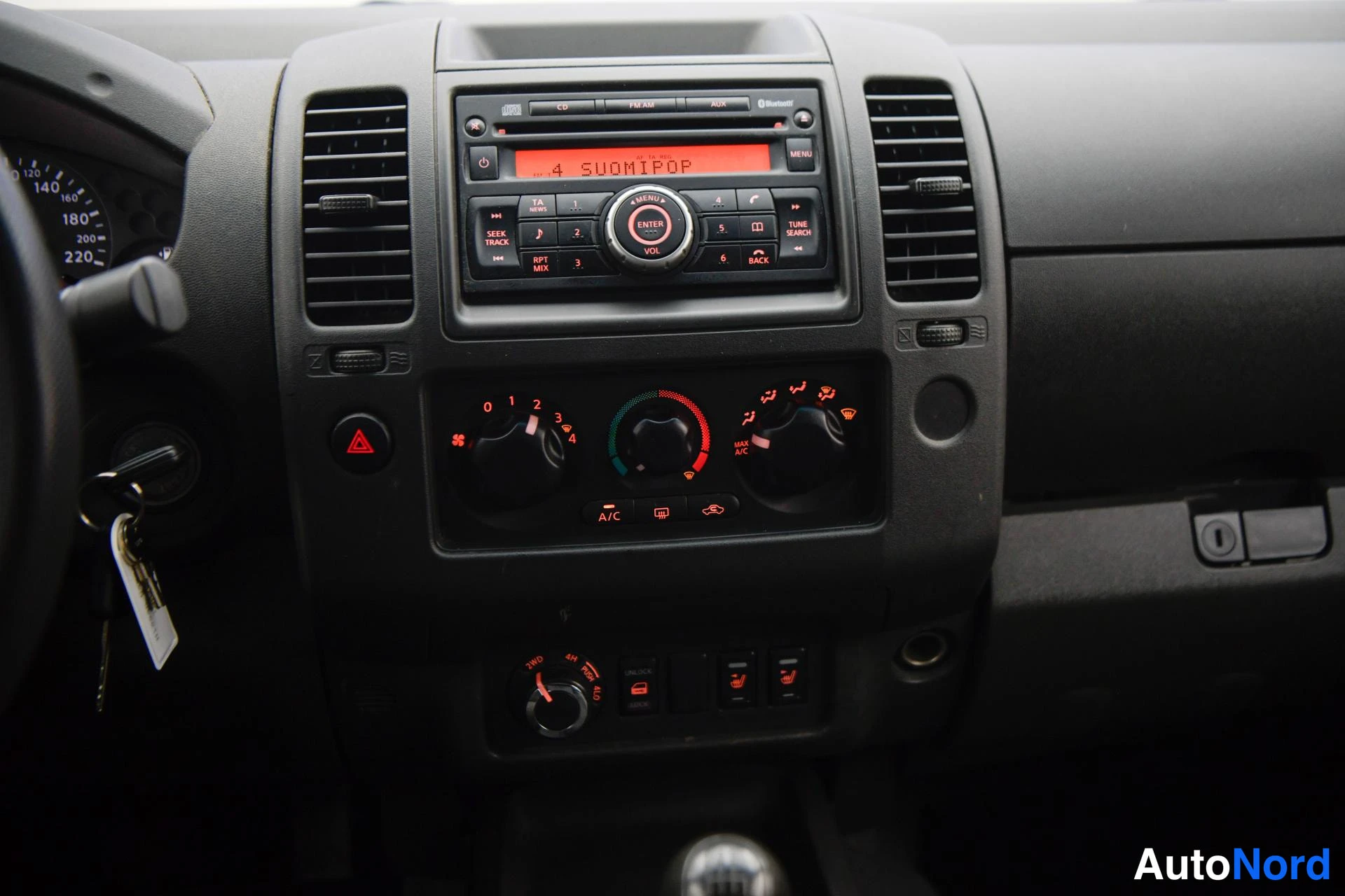 Muu: Kojelaudan keskiosan lähikuva: radiolaite näytöllä '4 SUOMIPOP', Bluetooth-merkintä, manuaaliset ilmastointisäätimet A/C-painikkeella ja kytkinlaakerin sytytysa