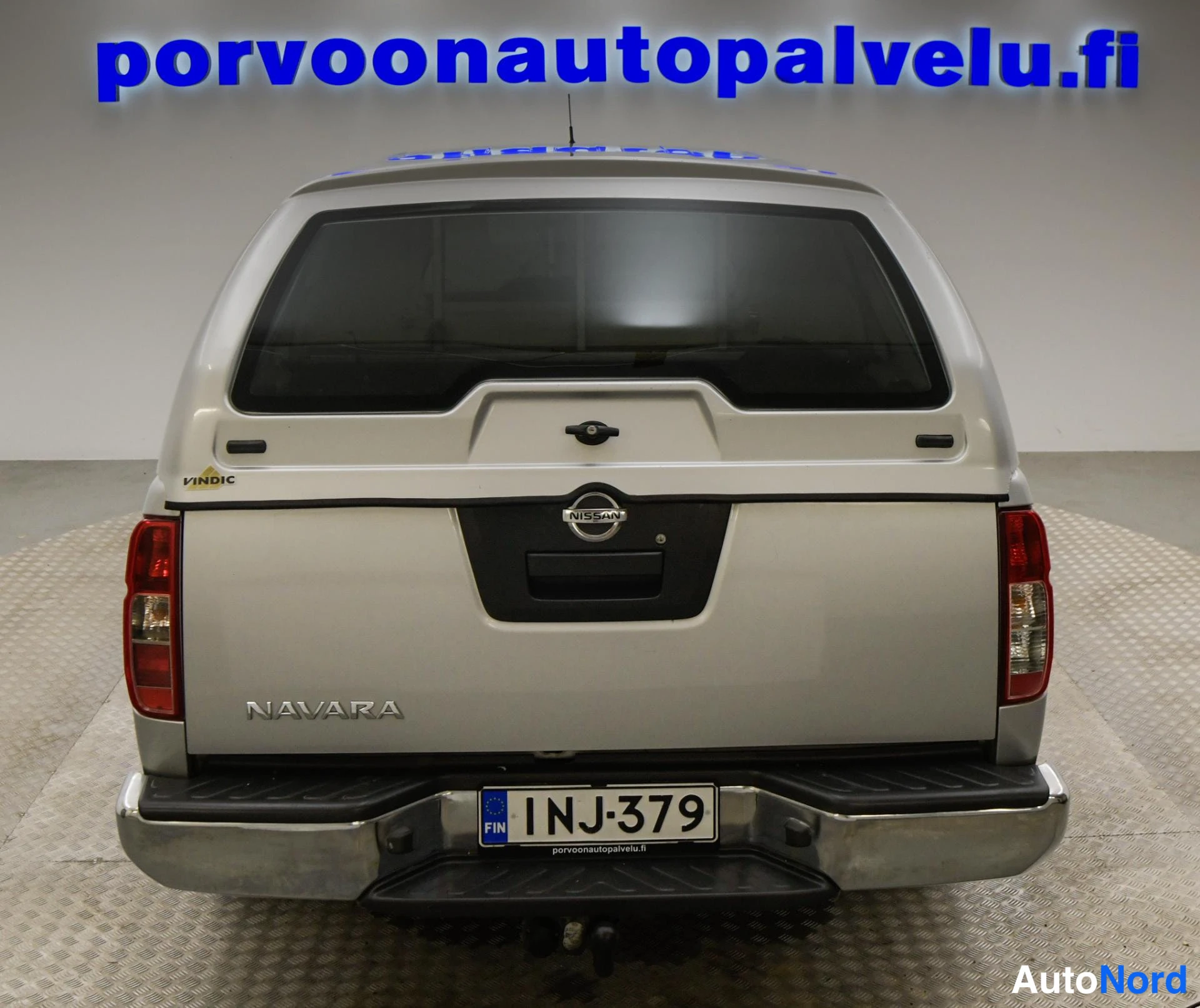 Takaa: Hopeanvärinen Nissan Navara suoraan takaa, NAVARA-takakirjain ja rekisteritunnus näkyvissä.