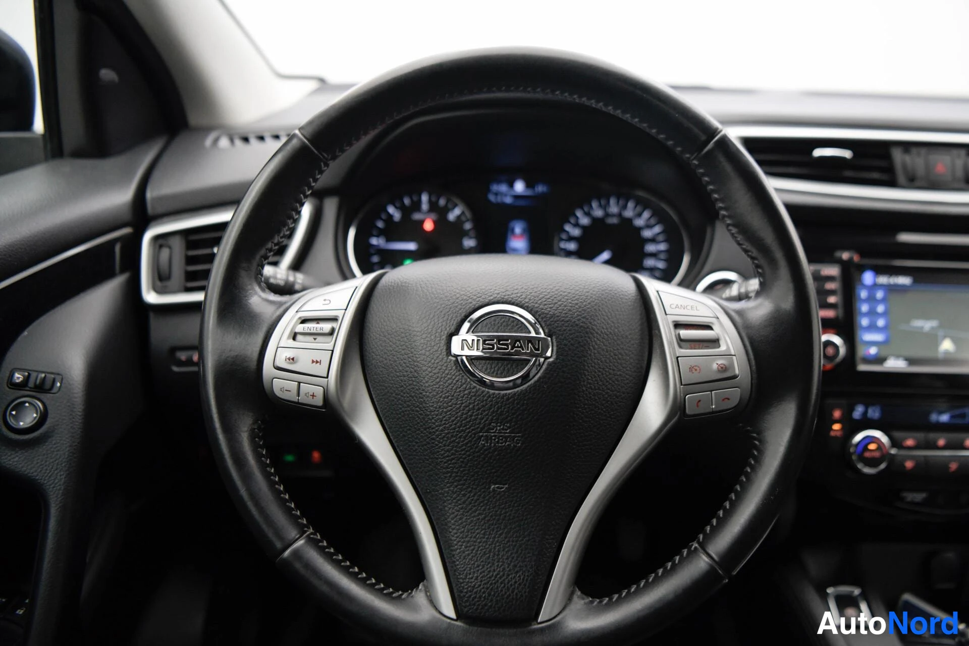 Muu: Nissan-ohjauspyörä lähikuvassa, mittaristo ja osa kosketusnäytöstä taustalla.