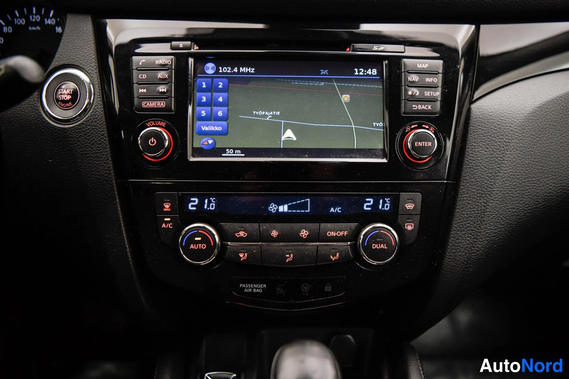 Muu: Keskikonsolin lähikuva: kosketusnäyttö näyttää radiota 102.4 MHz ja karttaa, ympärillä RADIO-, CD-, AUX-, MAP-, NAV- ja SETUP-napit. Start/Stop Engine -käynnist