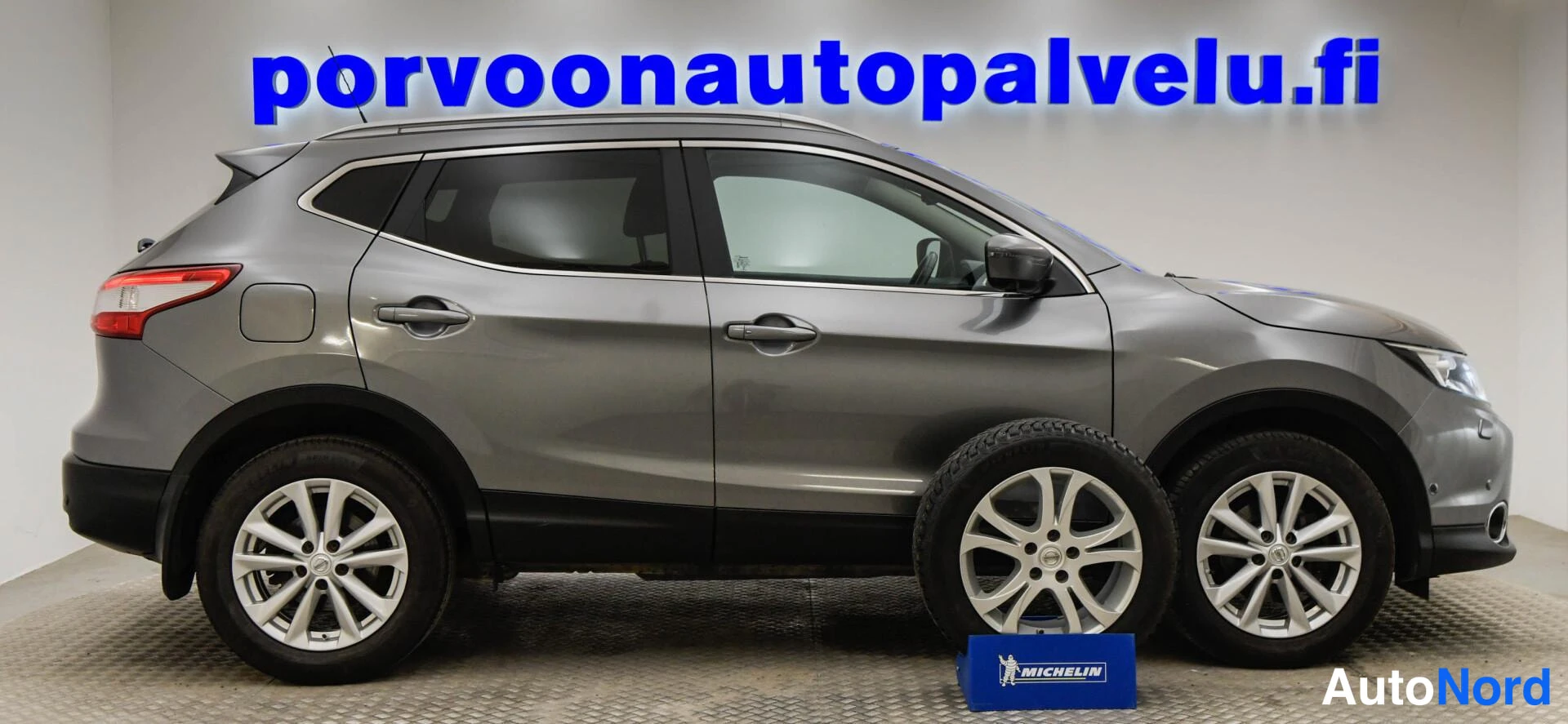 Etuviisto, nokka oikealle: Nissan Qashqai -katumaasturin sivuprofiili harmaana; oikeaan reunaan kytketty etupää ja edessä talvipyörä Michelin-telineessä.
