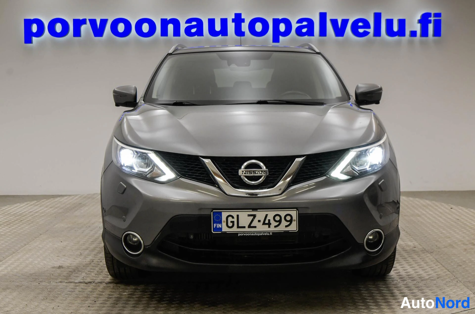 Edestä: Nissan Qashqai -katumaasturin suora etunäkymä, ajovalot päällä ja rekisterikilpi.