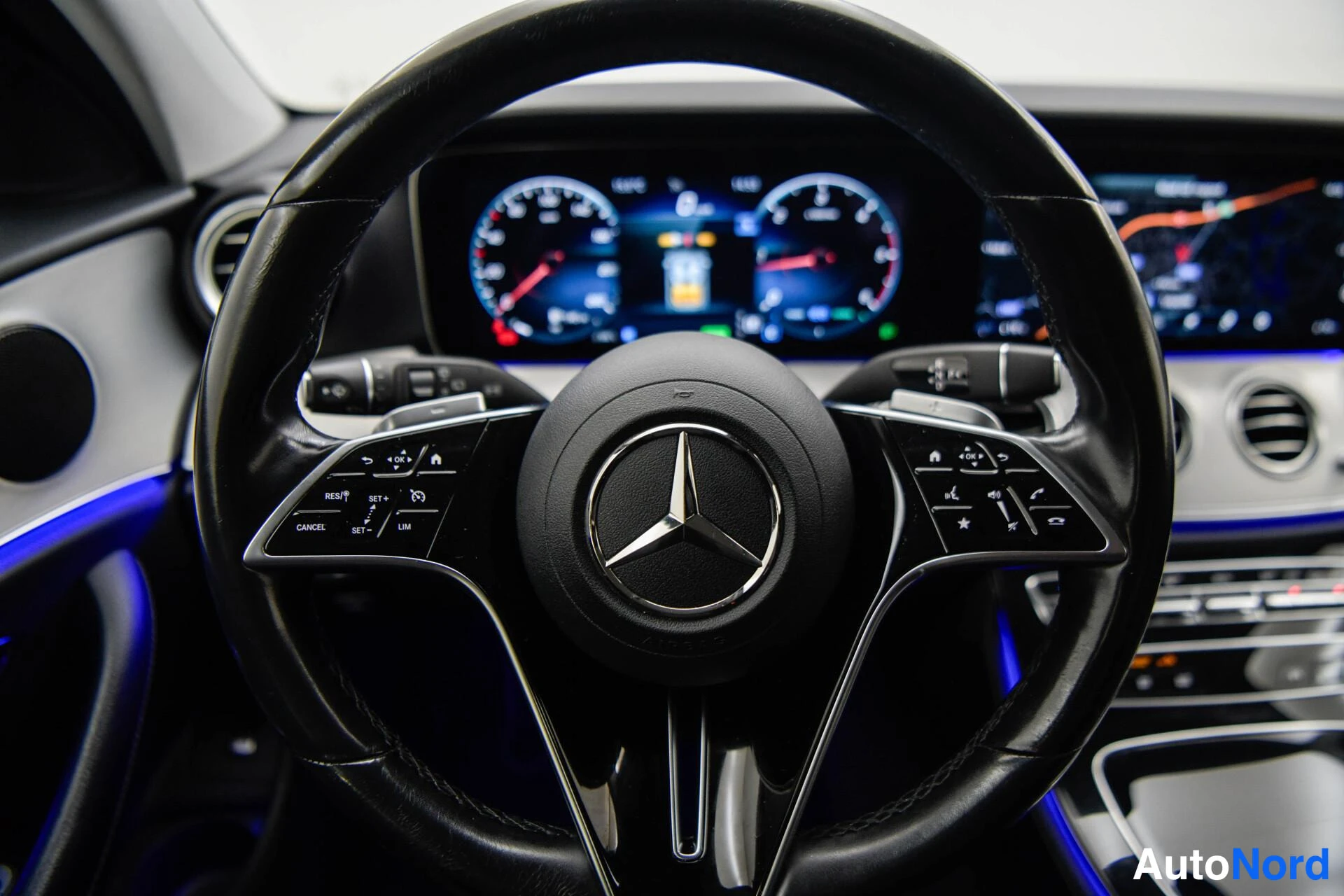 Muu: Mercedes-Benzin ohjauspyörä ja digitaalinen mittaristo lähikuvassa; näkymätön taustalla karttanäyttö ja ilmastointisuuttimet.