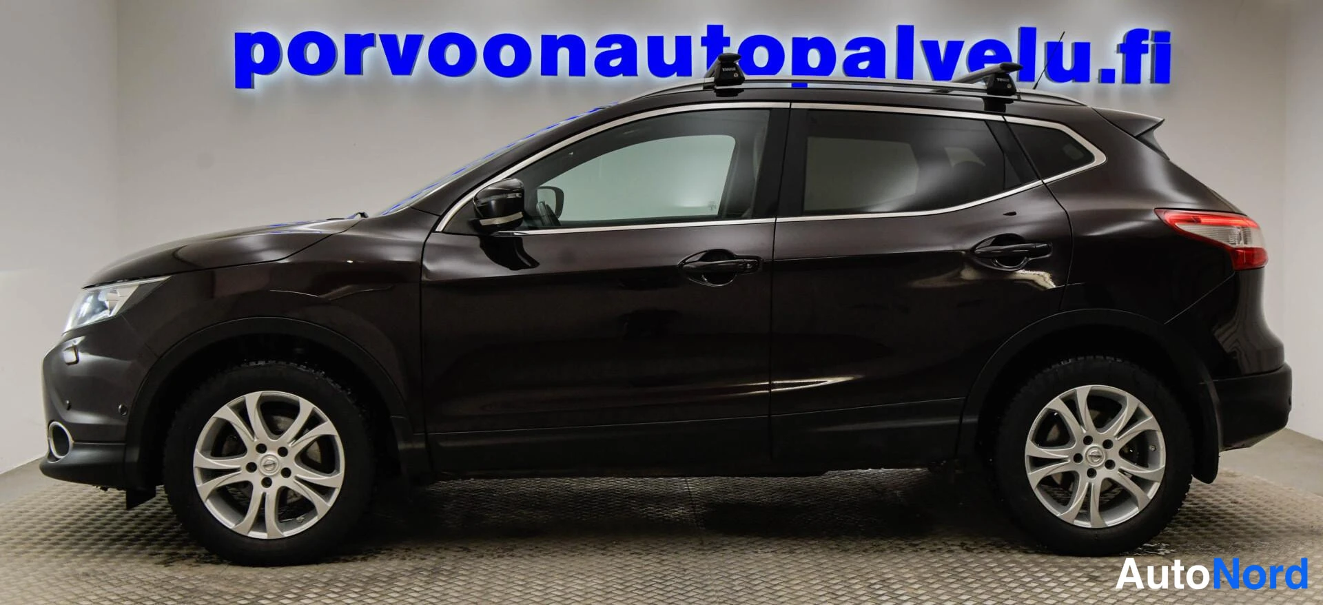 Takaviisto: Tummanruskea Nissan Qashqai sivulta vasemmalle kuvattuna; kyljen ovet, pyörät ja kattotelineet näkyvissä.