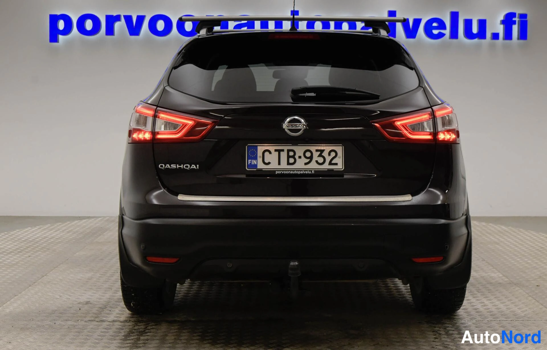 Takaa: Tummanruskea Nissan Qashqai suoraan takaa kuvattuna; takavalot palavat, QASHQAI-teksti ja rekisterikilpi näkyvissä.