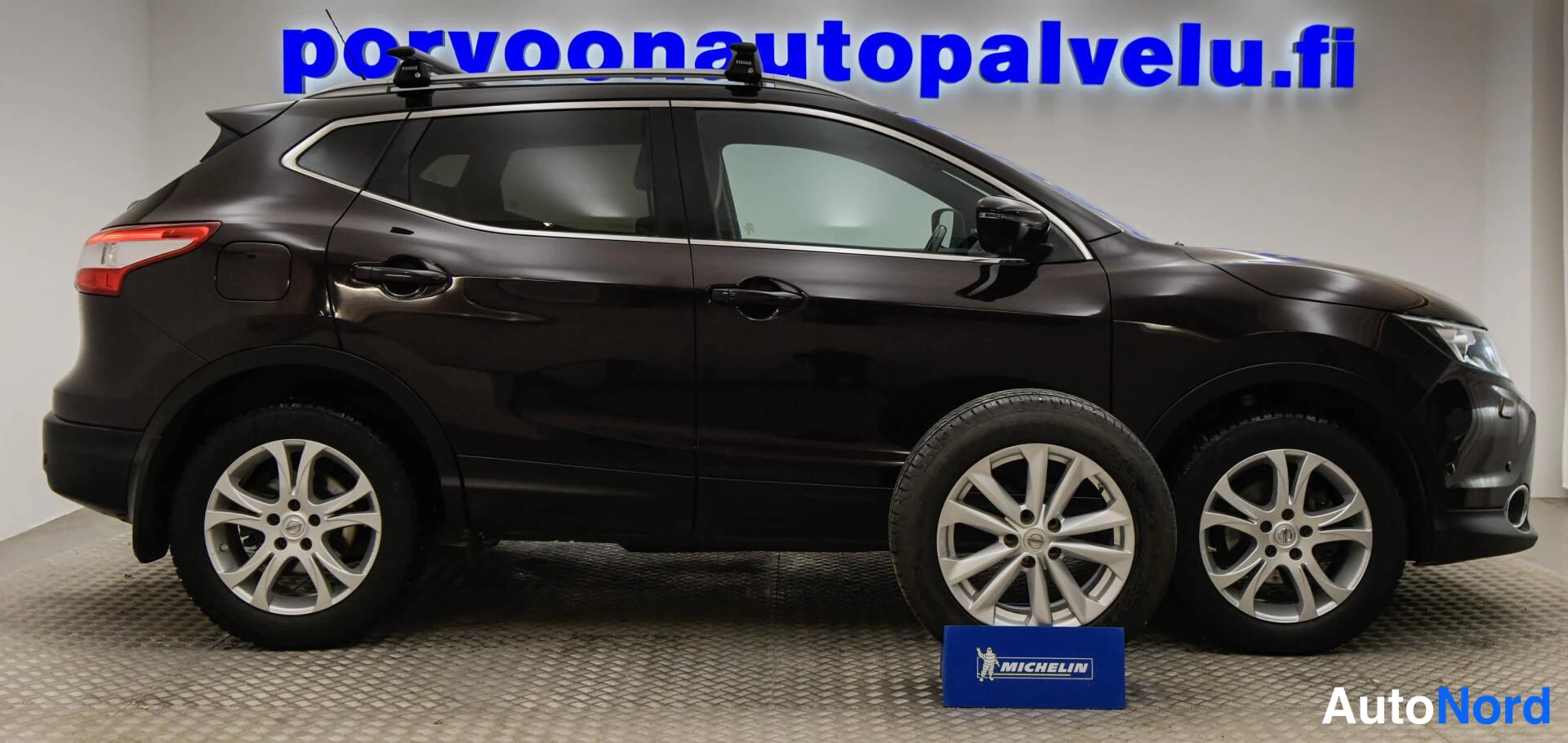 Etuviisto, nokka oikealle: Auton vasen kylki; tumma Nissan Qashqai kattotelineillä, renkaita ja neljä pyörää näkyvissä, Michelin-kyltti lattialla.