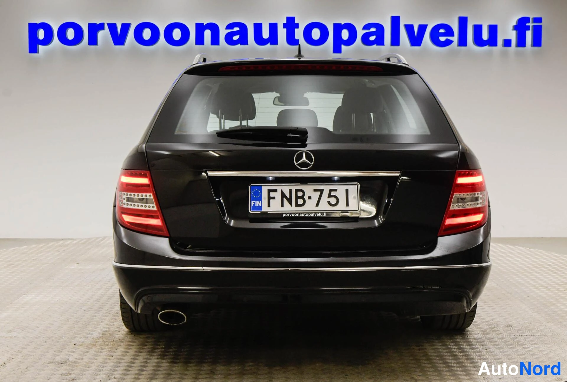 Takaa: Mustan farmariauton takaosa suoraan takaa kuvattuna; Mercedes-tähti, rekisteritunnus, takavalot ja pakoputki näkyvät.