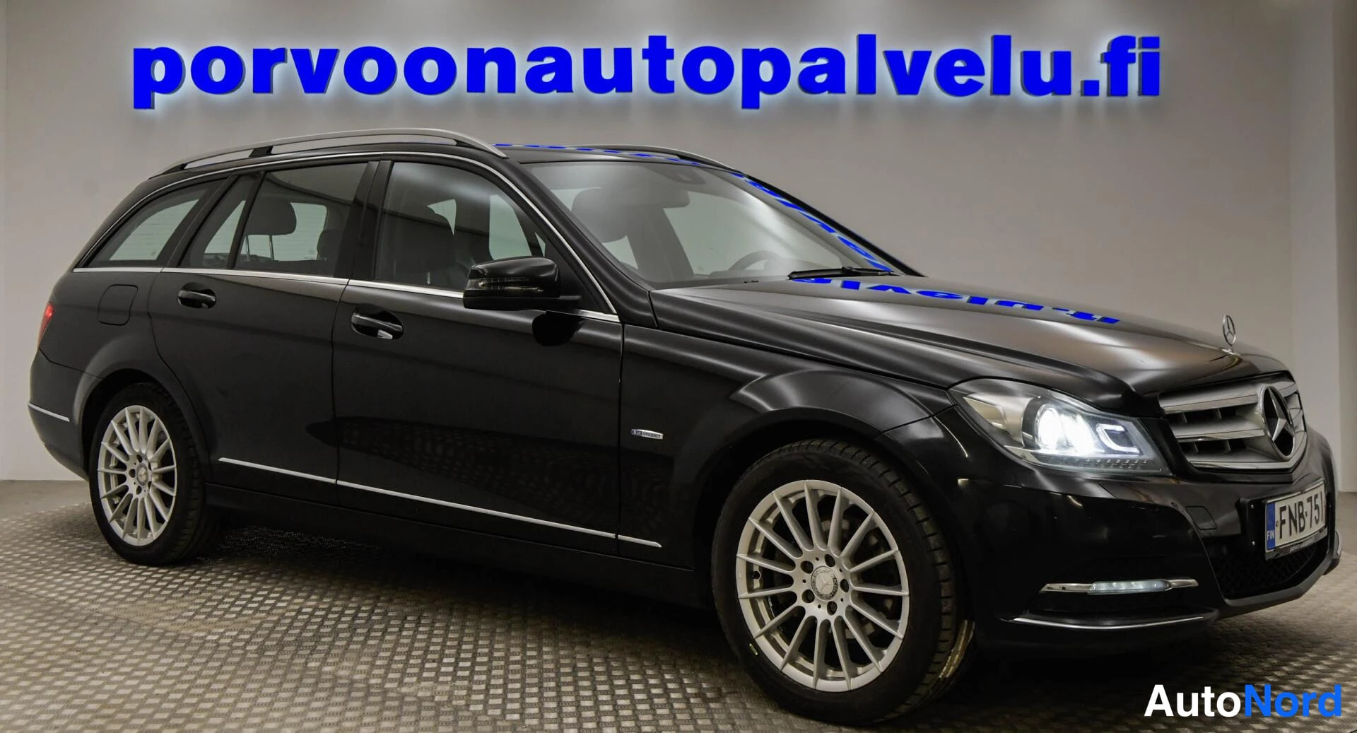Etuviisto, nokka oikealle: Mustan Mercedes-Benz C-sarjan farmarin etukulma oikealta, keulalla Mercedes-tähti ja rekisterikilpi, LED-ajovalot päällä.