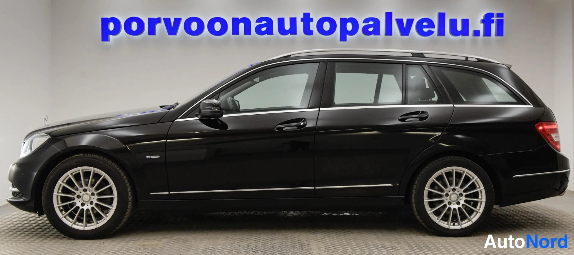 Takaviisto: Musta Mercedes-Benz C-sarjan farmari takakulmasta kuvattuna, takavalot ja kattokaiteet näkyvät, kylki kuvan oikealla puolella.