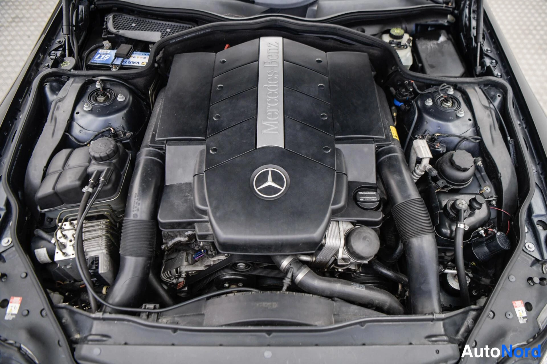 Muu: Avattu moottoritila, jossa Mercedes-Benz-merkintäinen tumma suojakansi ja V8-moottori.