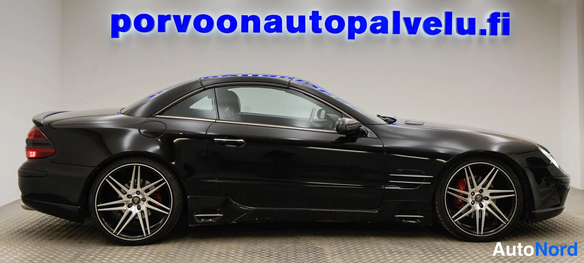 Takaviisto: Mustan Mercedes-Benz SL -henkilöauton takakulman ja sivuprofiilin näyttävä kuva sisätiloissa.