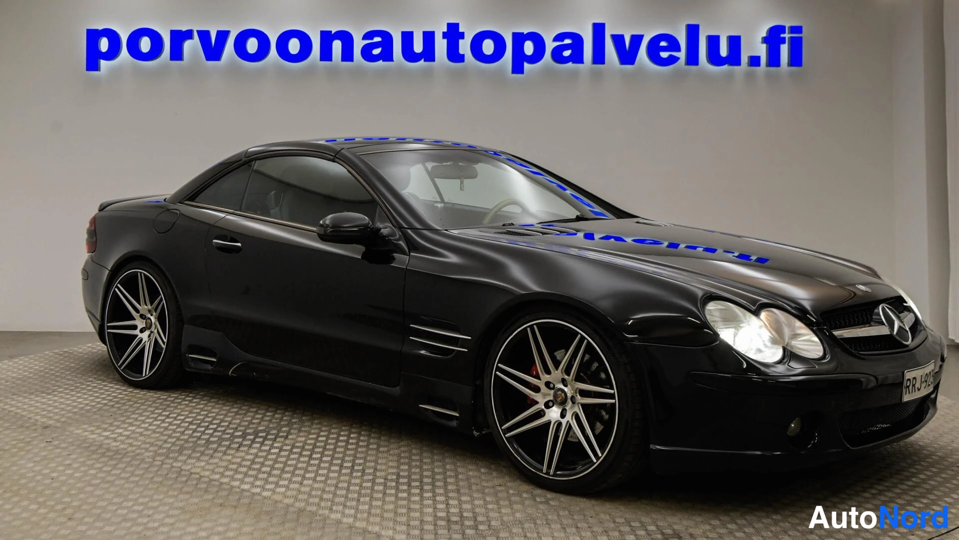 Etuviisto, nokka oikealle: Musta Mercedes-Benz SL -henkilöauto kulmassa edestä oikealta nähtynä sisätiloissa.