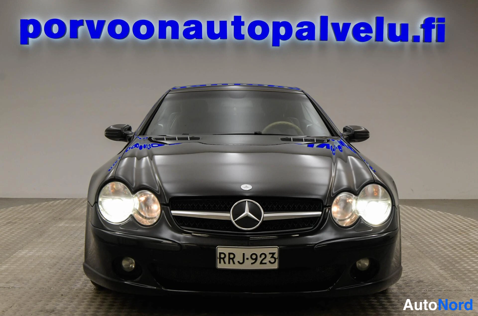 Edestä: Mustan Mercedes-Benz SL -henkilöauton edestäpäin otettu kuva sisätiloissa.