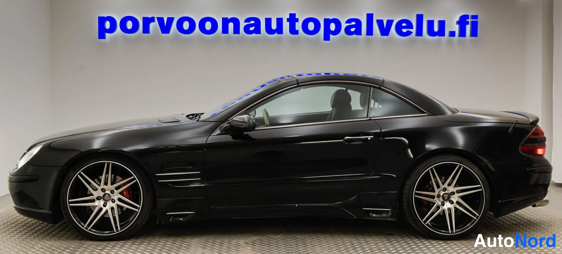 Takaviisto: Mustan Mercedes-Benz SL -henkilöauton takaosa ja sivuprofiili vasemmalta nähtynä sisätiloissa.
