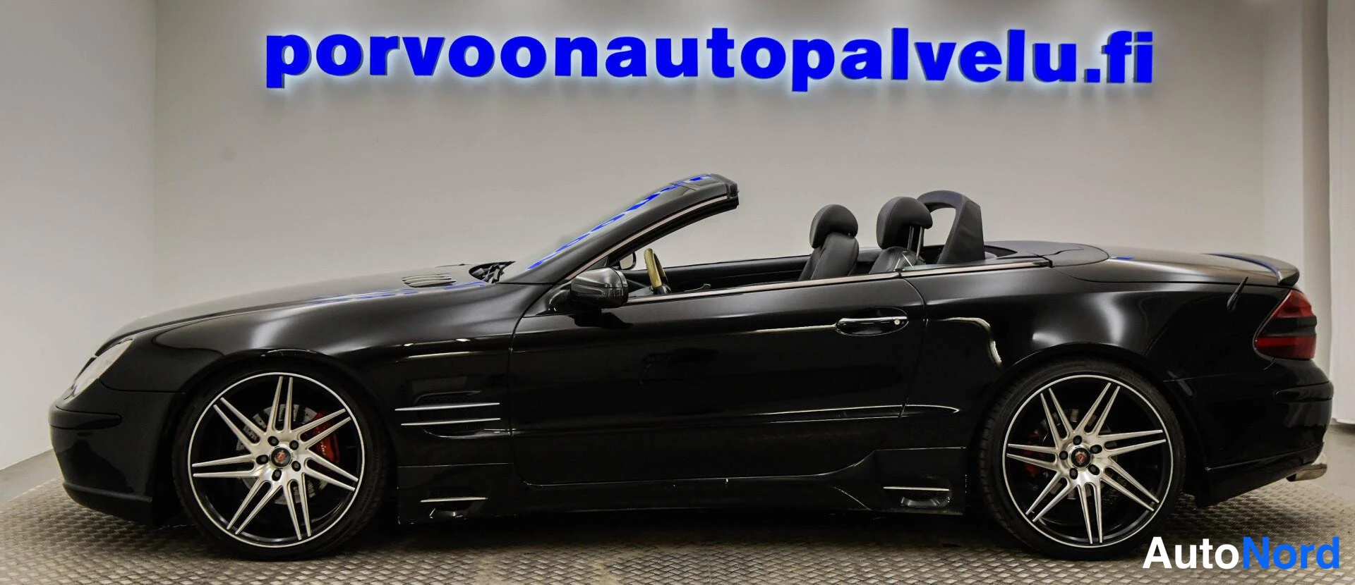 Etuviisto, nokka vasemmalle: Mustan avo-auton sivuvasen profiili, katto auki, isot monipuoliset kevytmetallivanteet.