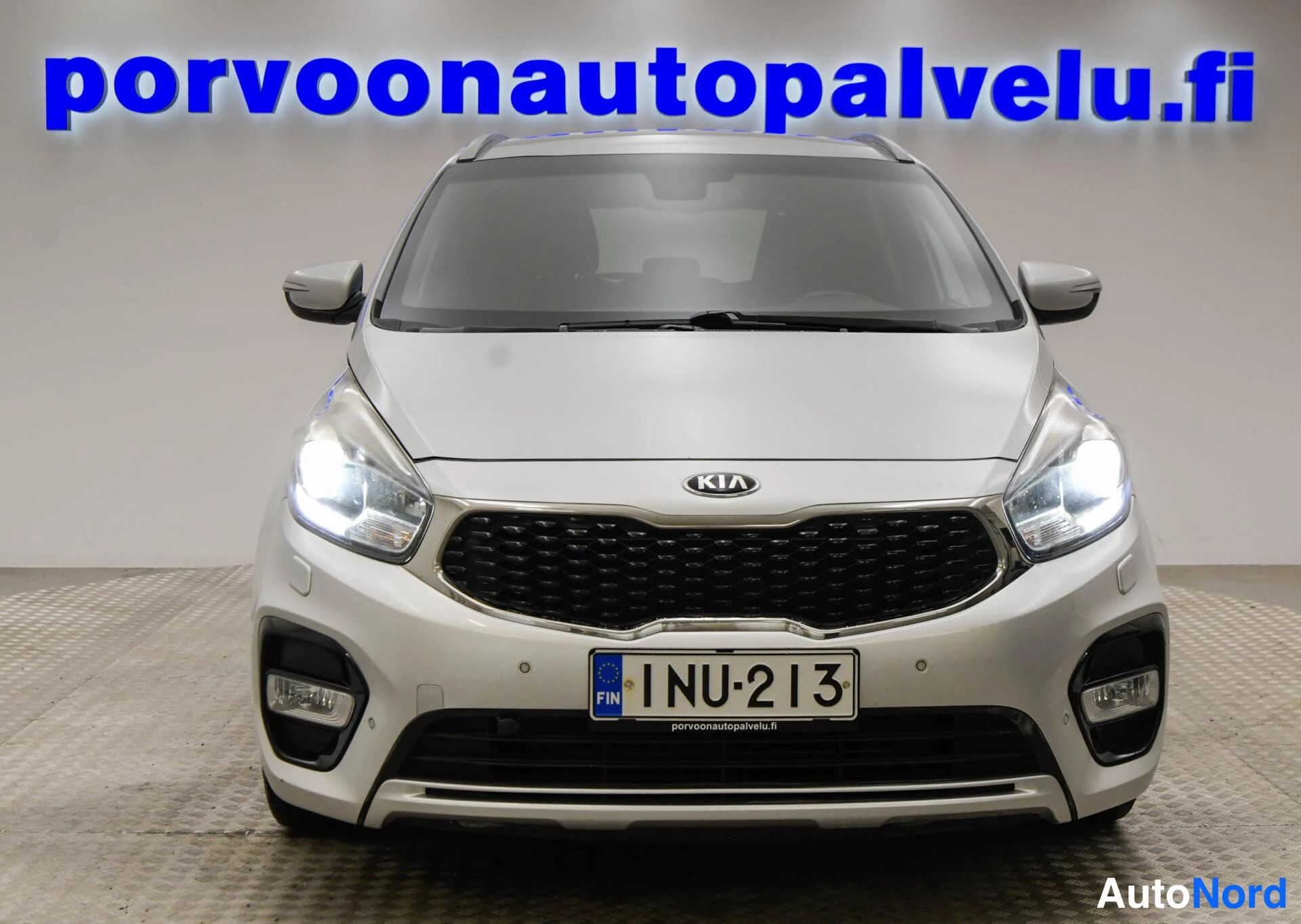 Edestä: Kia Carens suoraan edestäpäin, KIA-merkki ja rekisteritunnus.
