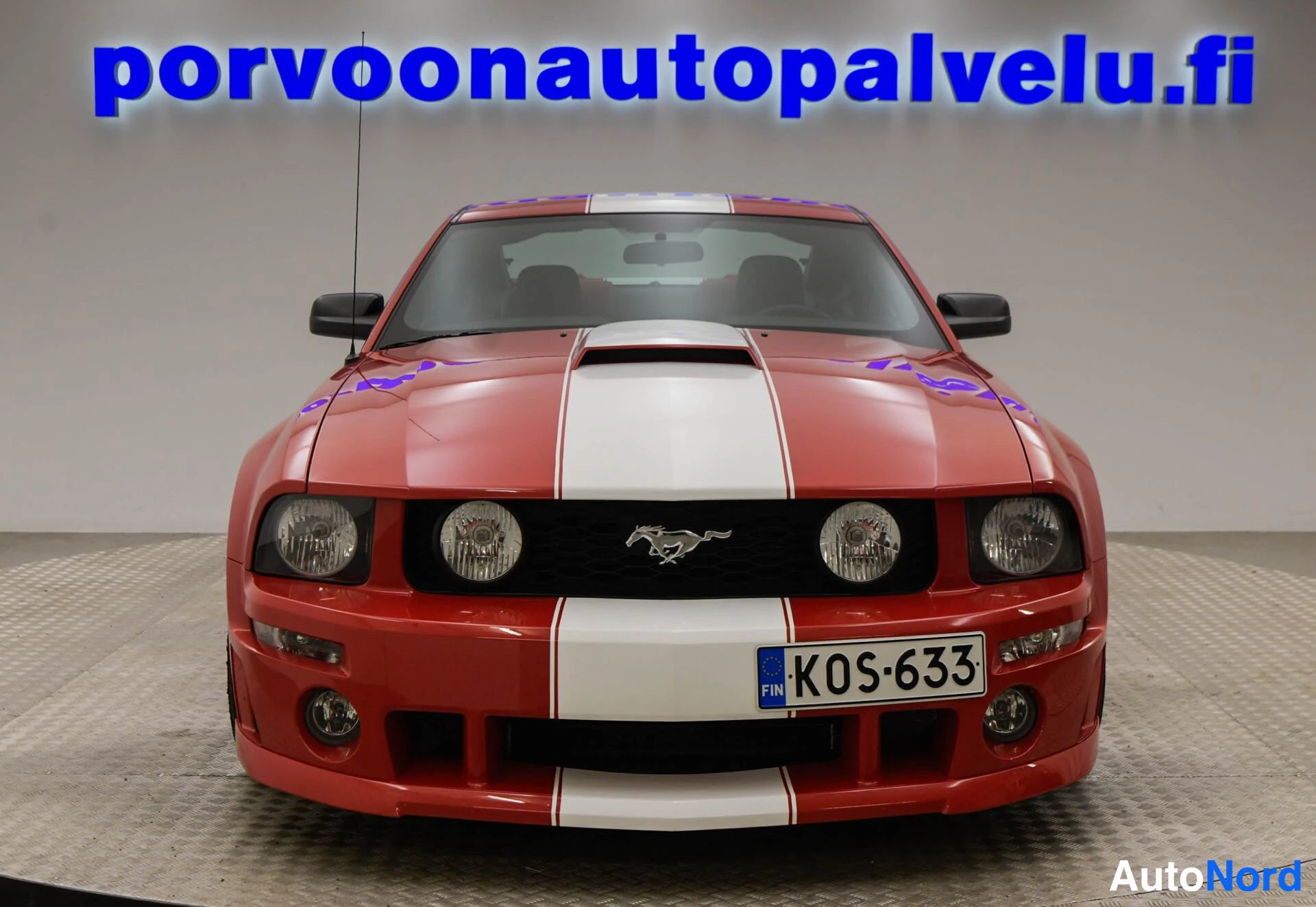 Edestä: Punaisen coupén etunäkymä, valkoinen raita konepellillä, Ford-merkki säleikössä ja -rekisterikilpi.