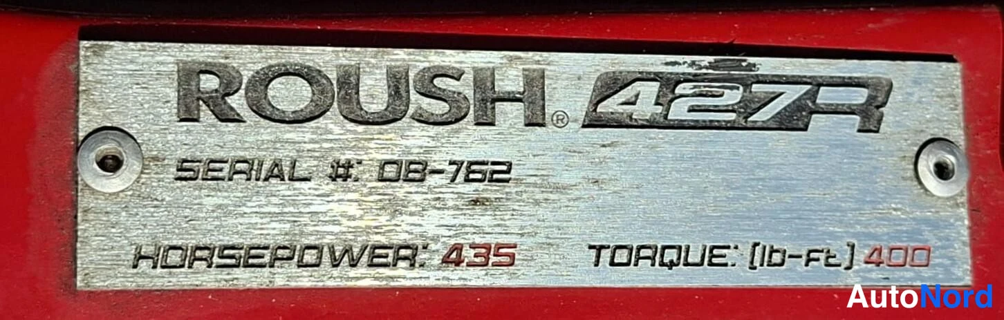 Yksityiskohta: Kulunut metallikilpi punaisella pohjalla: ROUSH 427R, SERIAL #: 08-762, HORSEPOWER: 435, TORQUE: (lb-ft) 400.