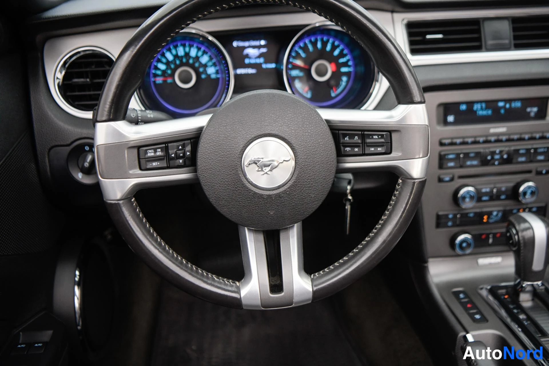 Yksityiskohta: Ohjauspyörän lähikuva Mustang-logolla, mitarit ja automaattivaihteen valitsin näkyvät.