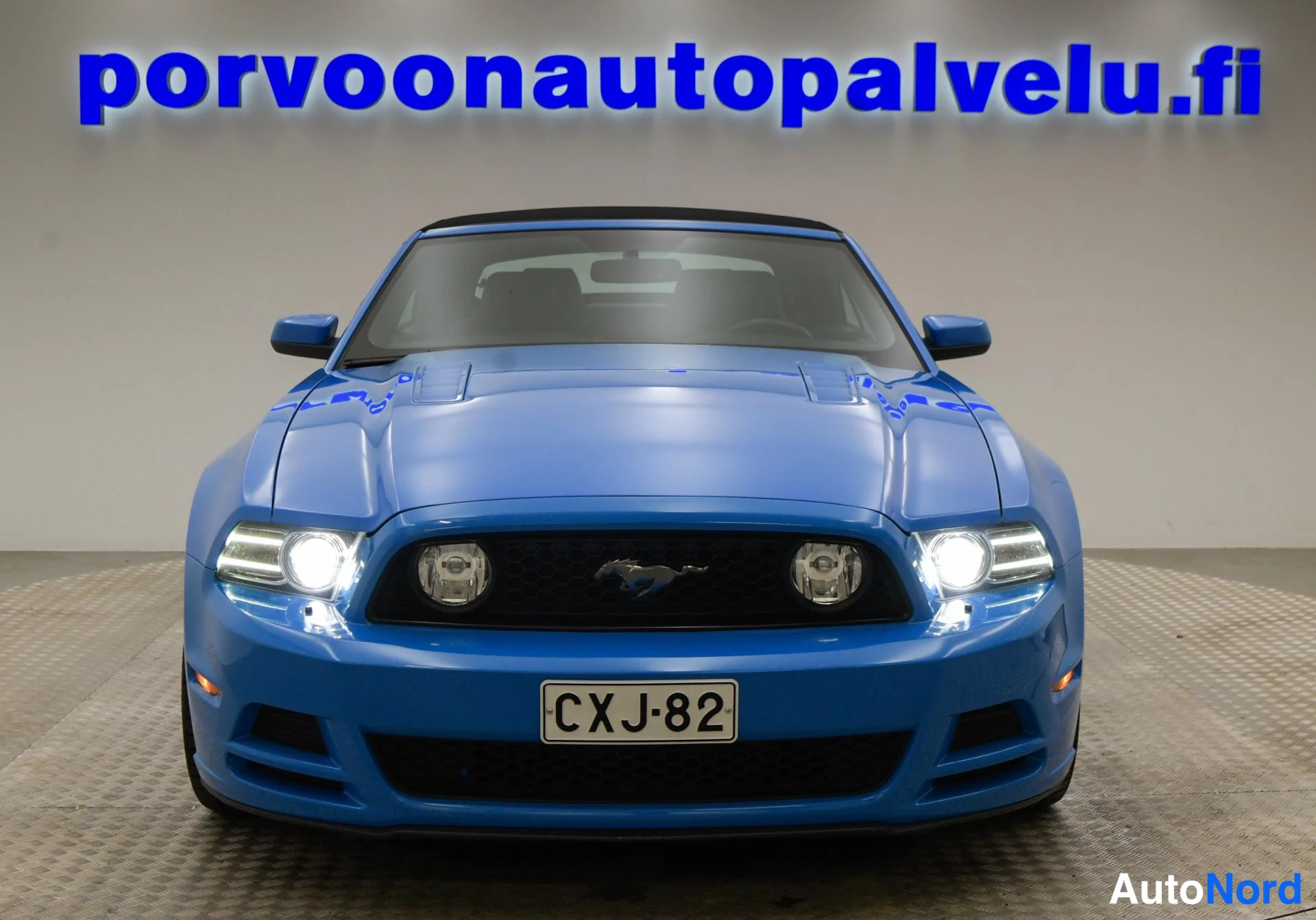 Edestä: Sininen Ford Mustang suoraan edestä kuvattuna, rekisterikilpi, ajovalot päällä