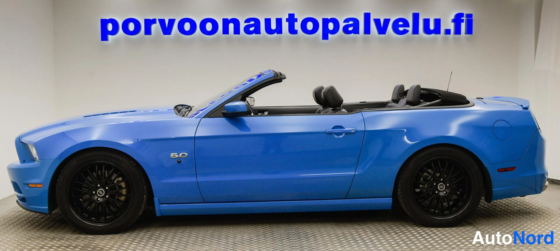 Sivulta: Sininen Ford Mustang -avonaisauto sivusta, 5.0-merkintä etulokasuojassa, mustat vanteet