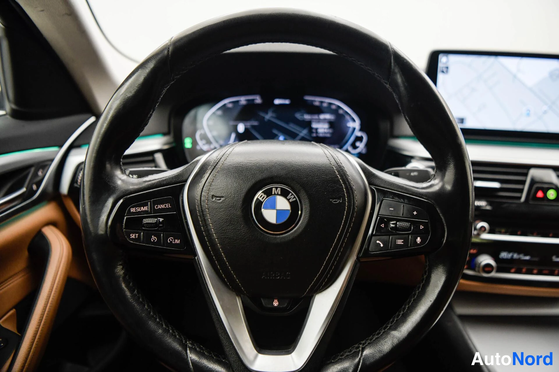 Edestä: Lähikuva BMW-ohjauspyörästä ja digitaalisesta mittaristosta, taustalla keskinäytön kartta ja ilmastointipaneeli.