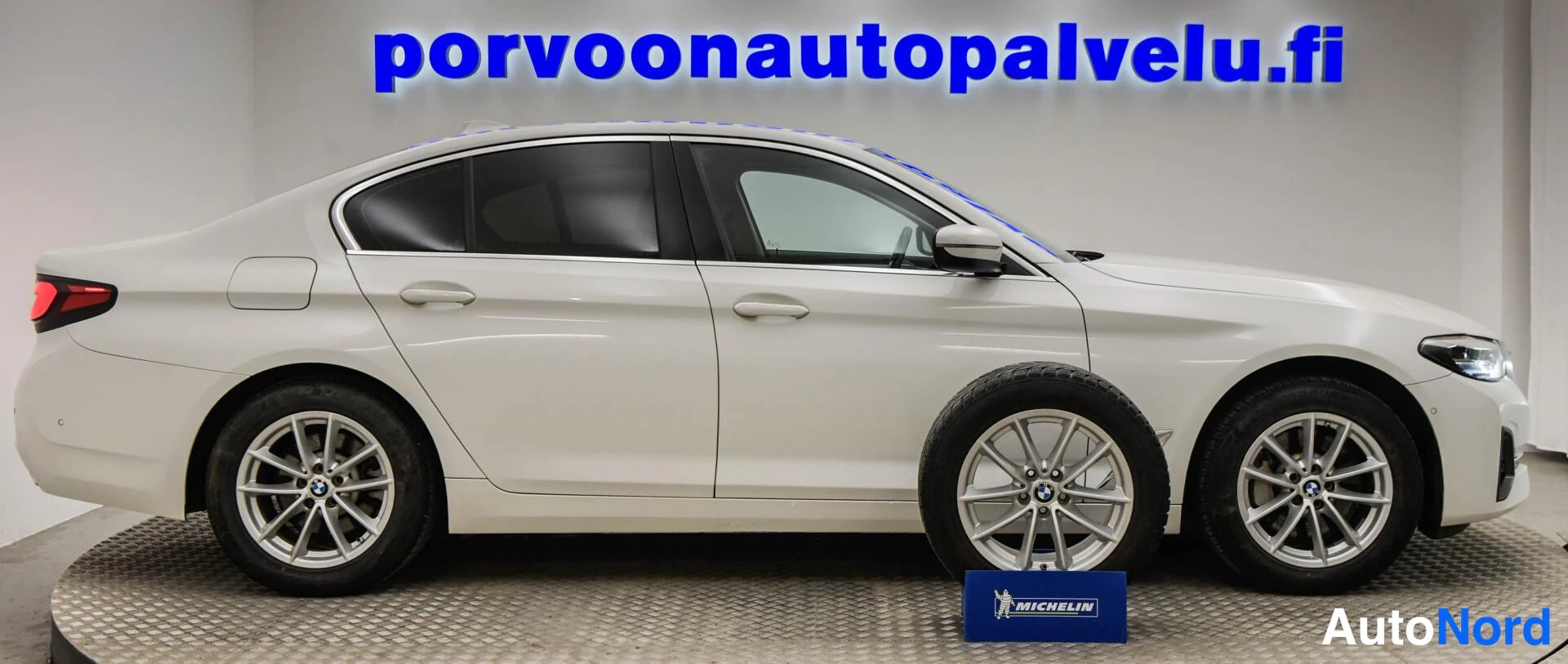 Etuviisto, nokka oikealle: Valkoinen BMW-sedan sivuprofiilissa; keulakko oikealla ja varapyörä esillä kuvan etualalla.