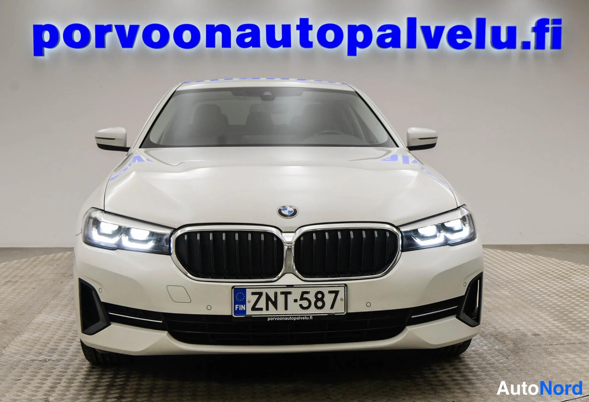 Edestä: Valkoinen BMW-sedan suora edestä; musta munuaismaski ja rekisterikilpi.