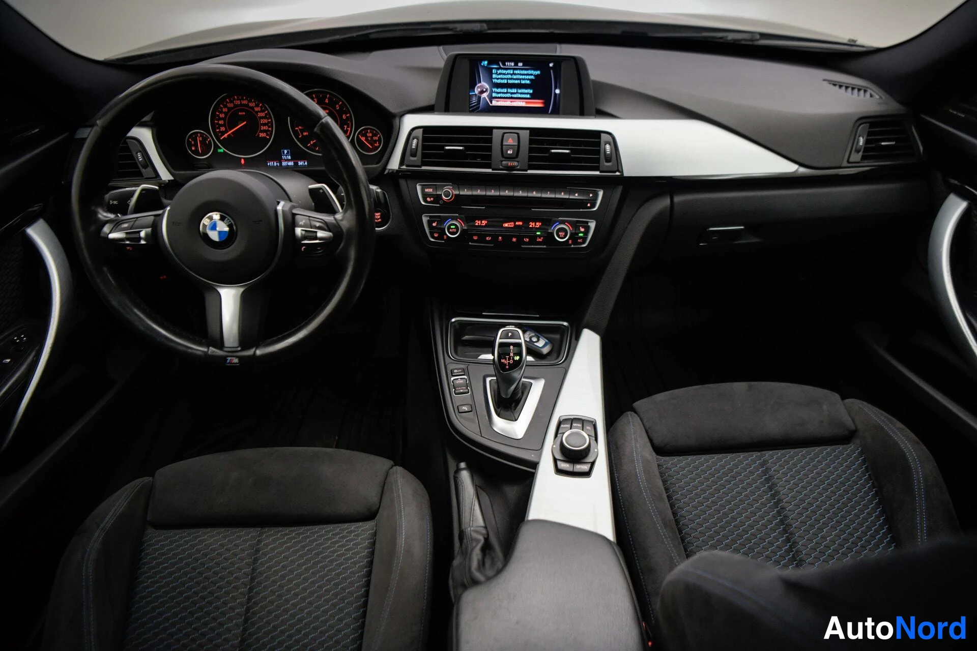 Muu: BMW:n kojelauta edestä: ohjauspyörä, mittarit, infonäyttö, ilmastointipaneeli ja vaihtaja.