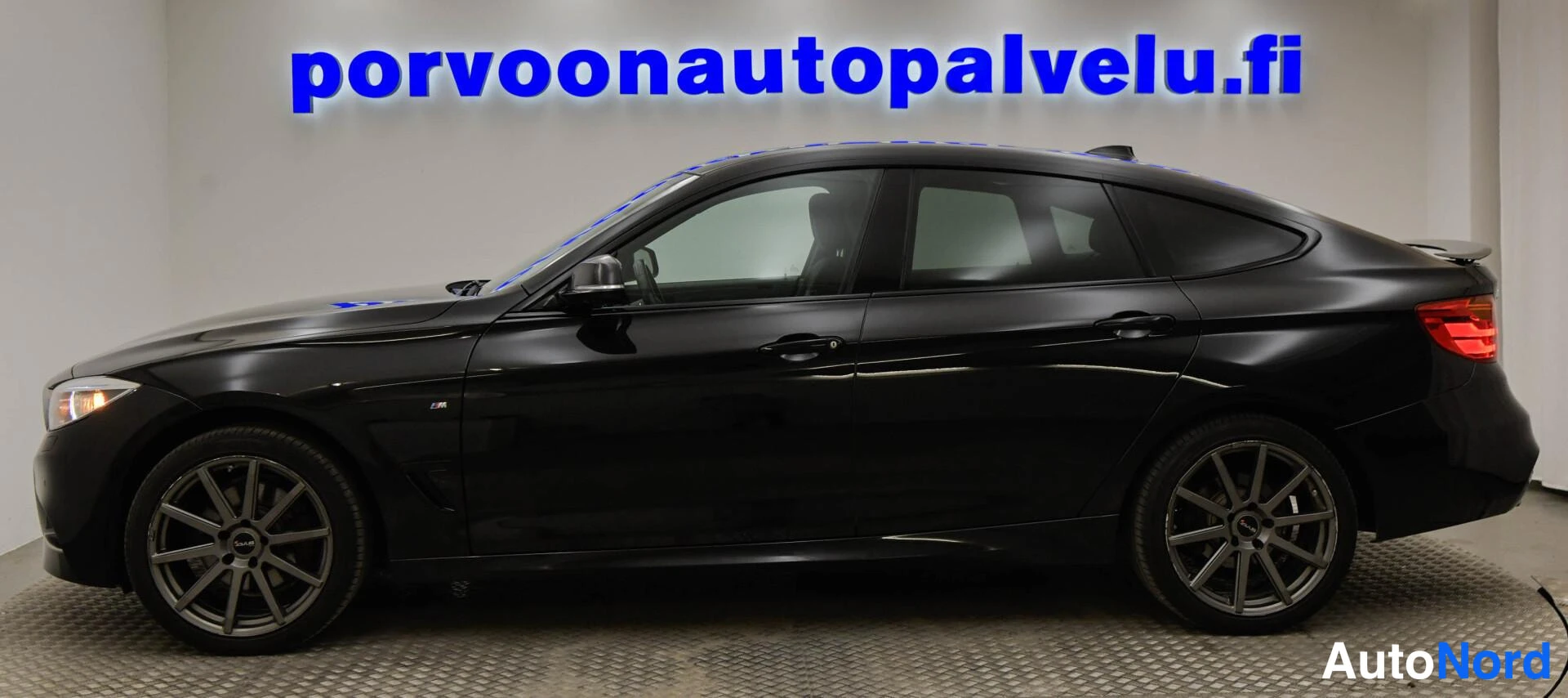 Etuviisto, nokka vasemmalle: Mustan BMW:n kulmaustakuva etupuolelta vasemmalta: etusäleikkö ja vasen sivu näkyvät, auton koko runko tummansinimusta.
