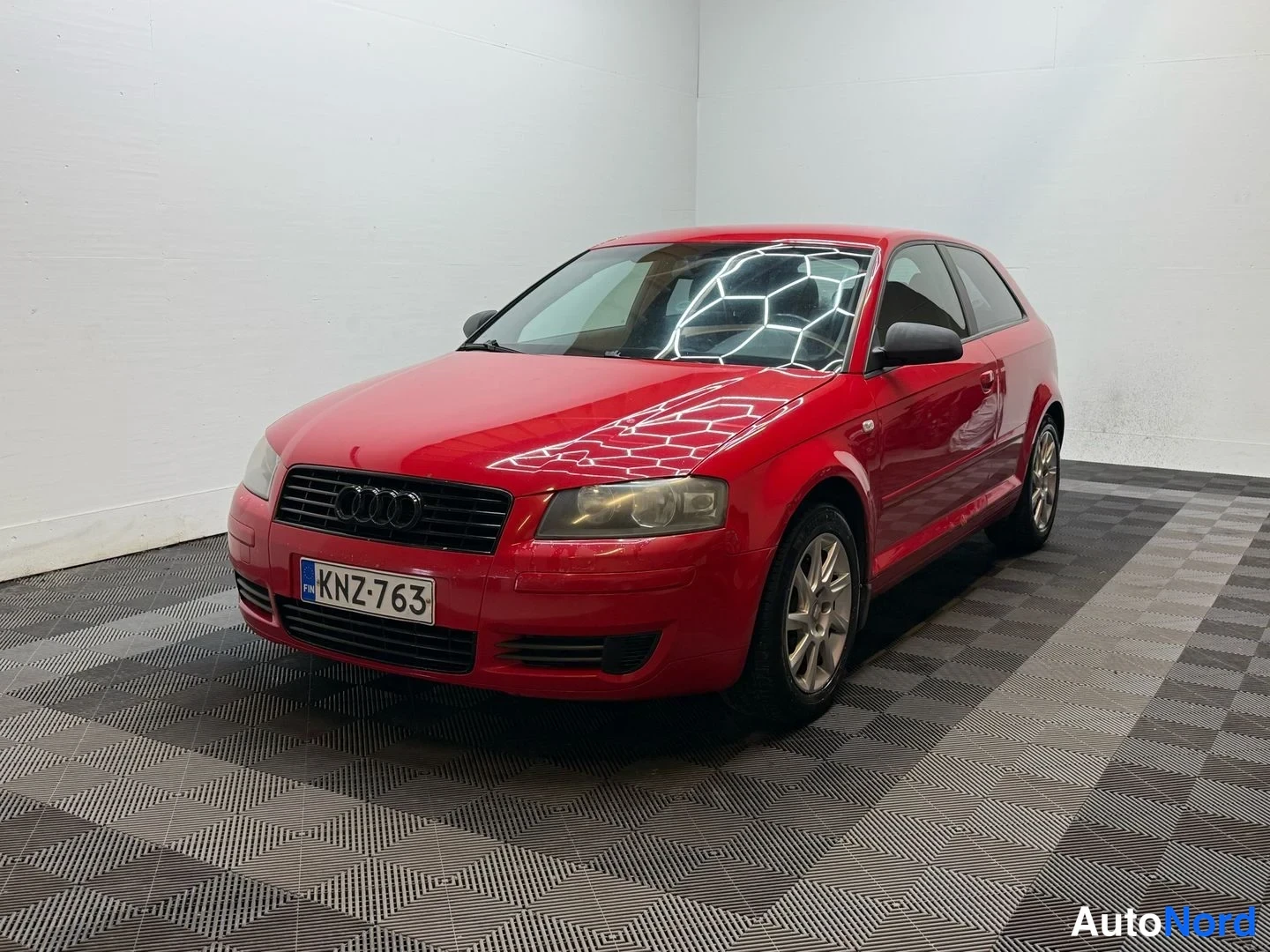 Etuviisto, nokka vasemmalle: Punainen Audi A3 3-ovinen etukulmasta, rekisteritunnus.