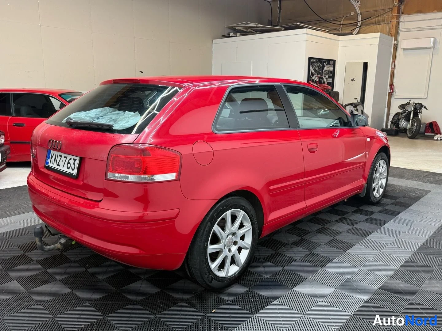 Takaviisto: Audi A3 Sportback, punainen, takakulmanäkymä vasemmalta; rekisterikilpi, takavalot, vetokoulu ja alumiinivanteet näkyvät hallissa.
