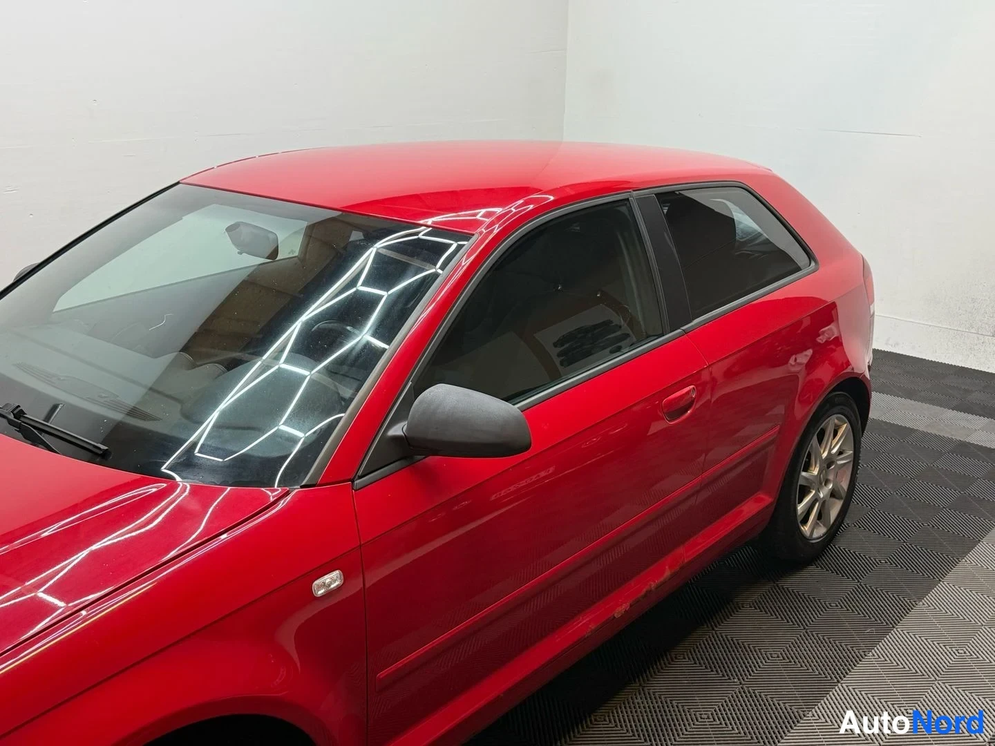 Sivulta: Audi A3 Sportbackin oikea kylki punaisena; ovien kahvat, ulkotakipeili ja muovivanteet näkyvät sisätilassa.