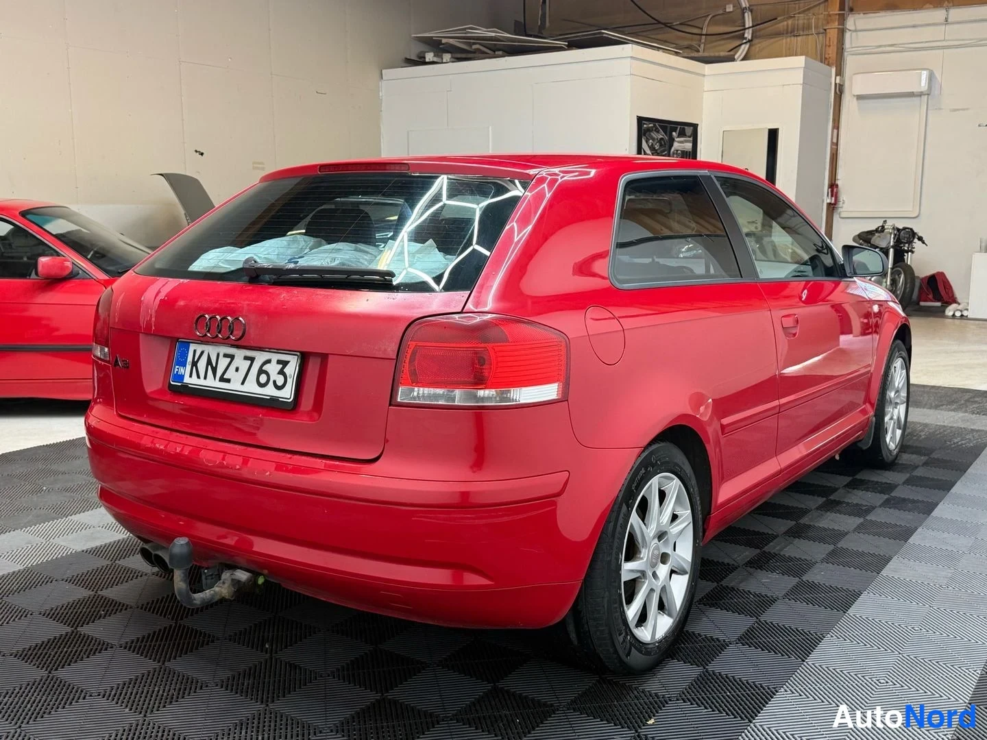 Takaviisto: Audi A3 Sportback, punainen, takakulmanäkymä vasemmalta; rekisterikilpi, takavalot, vetokoulu ja alumiinivanteet näkyvät hallissa.