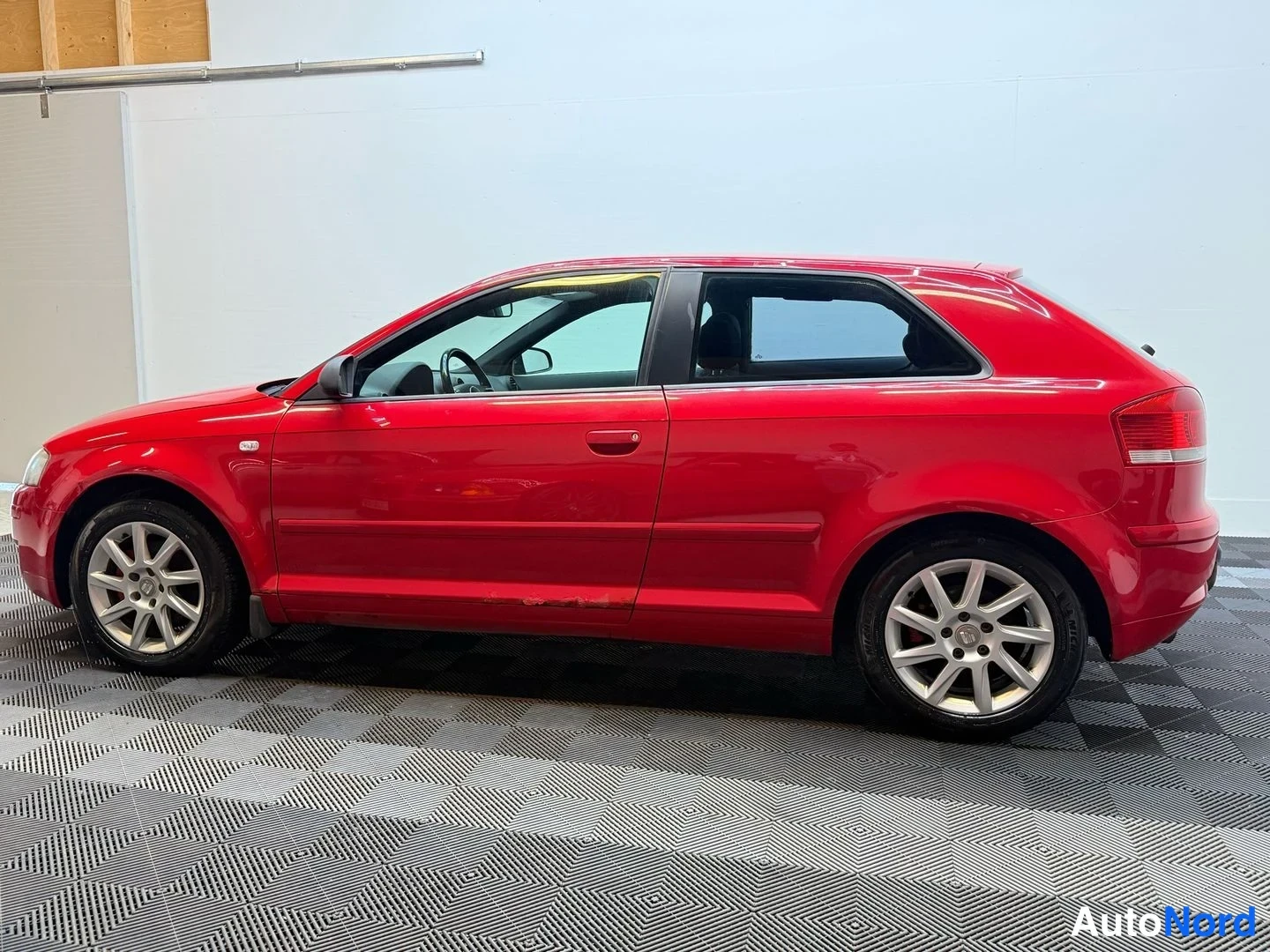 Takaviisto: Audi A3 Sportback, punainen kolmiovinen viistotakakulma sisätiloissa; takavalo ja takapuskuri sekä vasen sivu näkyvät kokonaan.