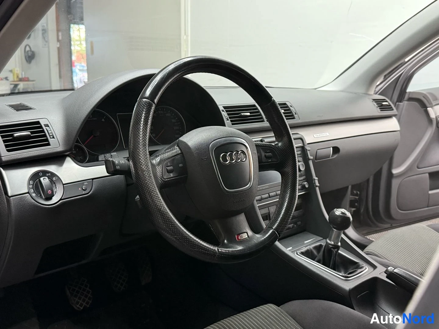 Edestä: Ohjaamo vasemmalta: musta, kulunut Audi-ohjauspyörä, käsivalintainen vaihtaja ja tumma kojelauta.