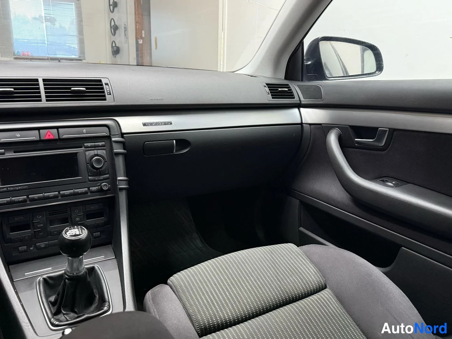 Muu: Audi A4:n sisätilat: kojelauta, manuaalivaihteisto, radionäyttö ja matkustajan ovipaneeli.