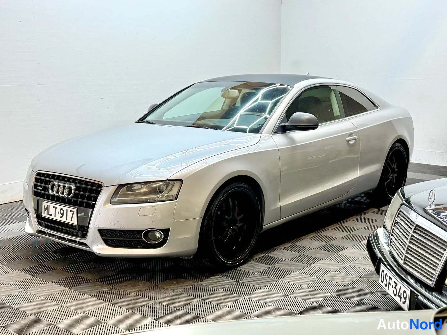 Etuviisto, nokka vasemmalle: Audi A5 -kupéHopeanvärinen henkilöauto sisätiloissa, etukulmanäky, rekisteritunnus, mustat kevytmetallivanteet.