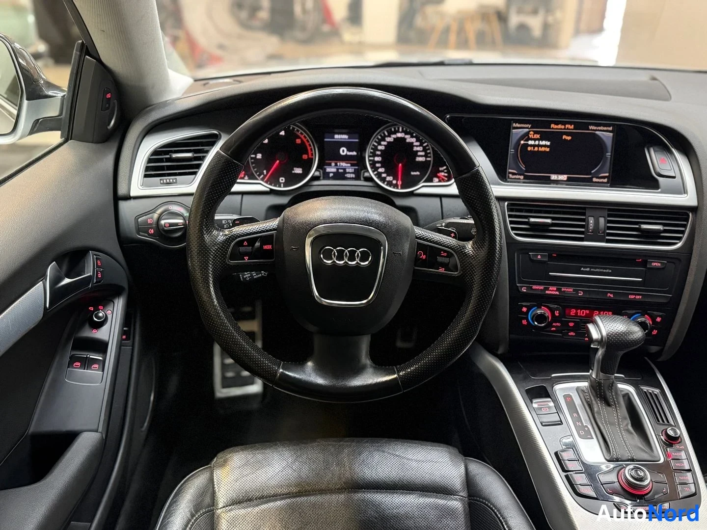 Muu: Ohjauspisteen näkymä: Audi-ohjauspyörä, digitaalinen mittaristo 0 km/h ja keskinäytön radiotiedot.