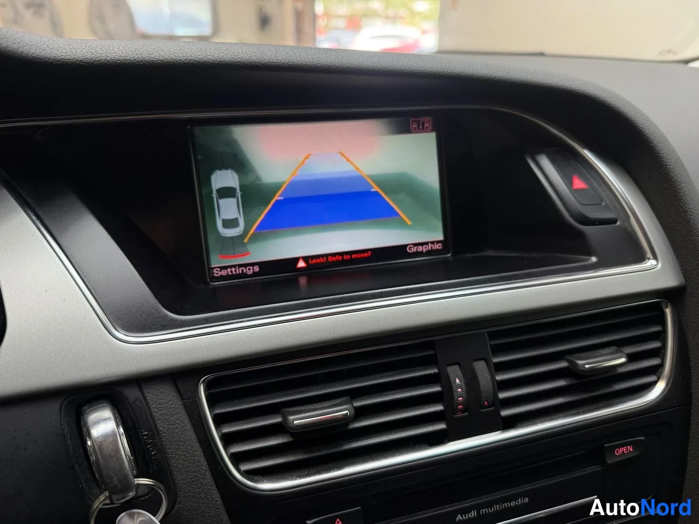 Muu: Sisätilakuva: infotainment-näytöllä pysäköintigrafiikka ohjausviivoineen, teksti 'Look! Safe to move?' näkyvissä.