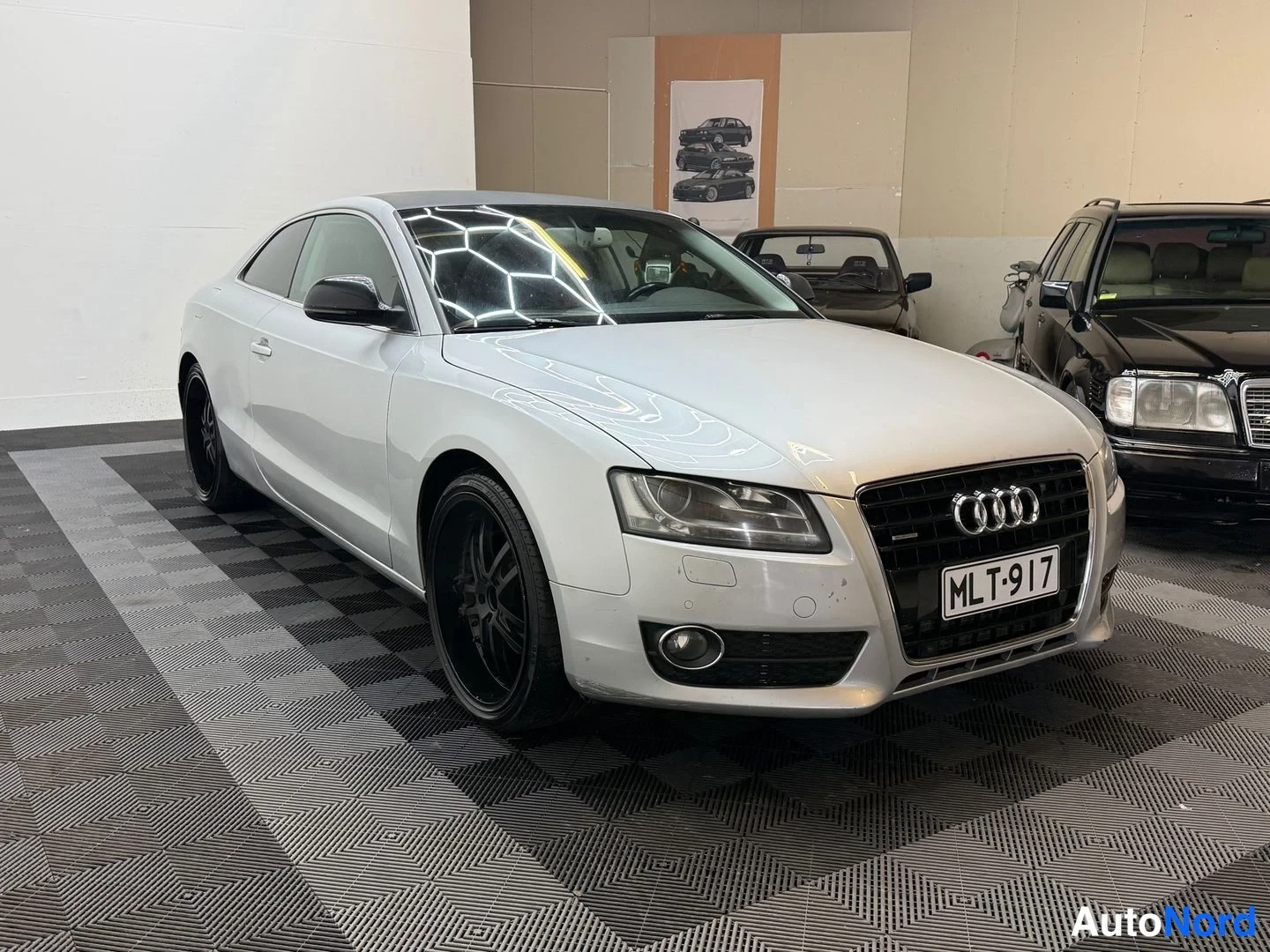 Etuviisto, nokka oikealle: Audi A5 -kupéHopeanvärinen henkilöauto sisätiloissa, etukulmanäky oikealta, rekisteritunnus, mustat kevytmetallivanteet.